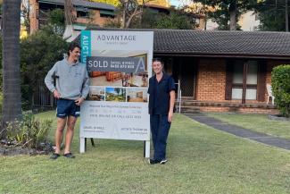 Image of Flynn and Heidi with the 'sold' sign at their newly purchased property